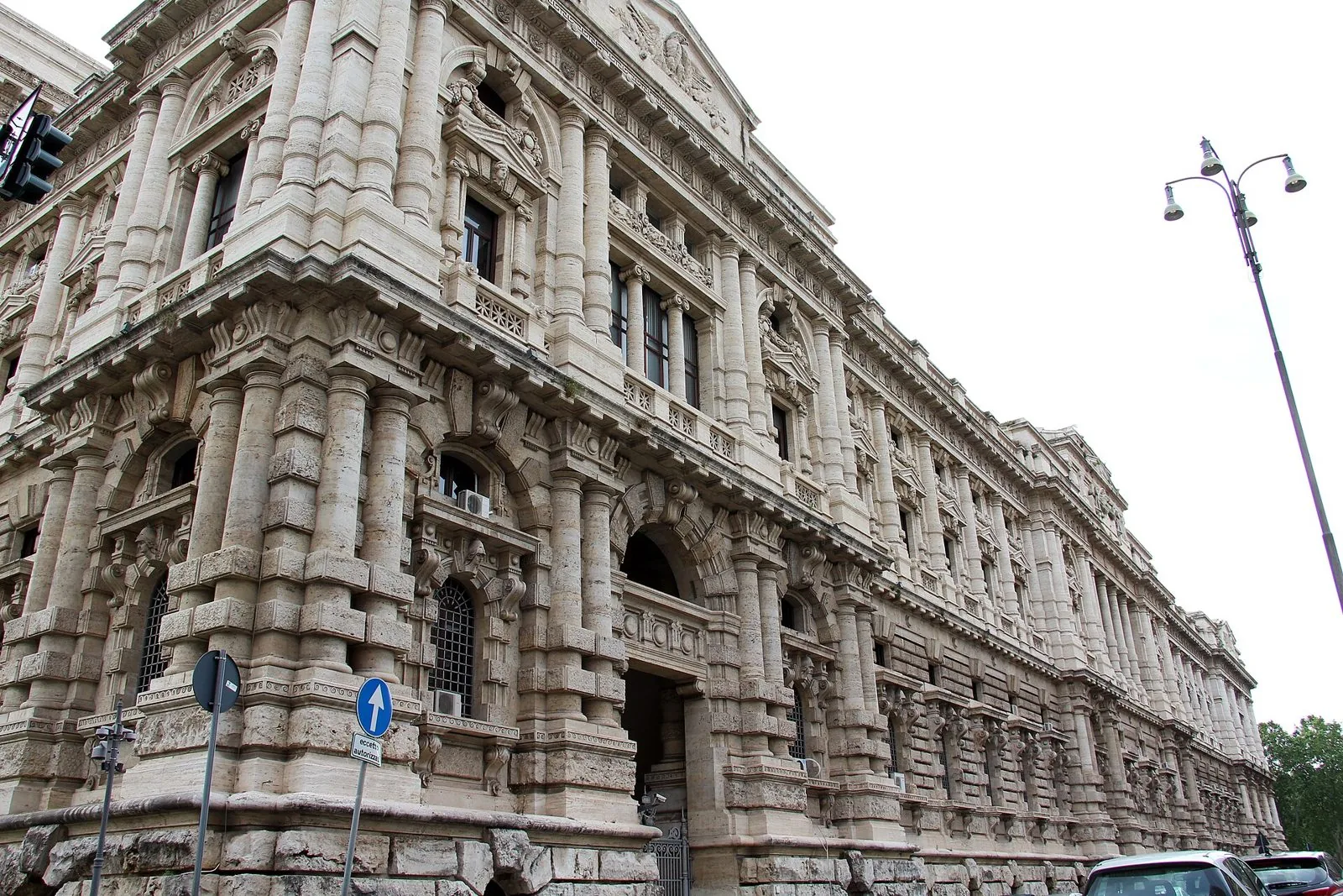 La facciata laterale in travertino del Palazzo di Giustizia di Roma, con colonne, finestre decorate e un lampione, sotto un cielo chiaro