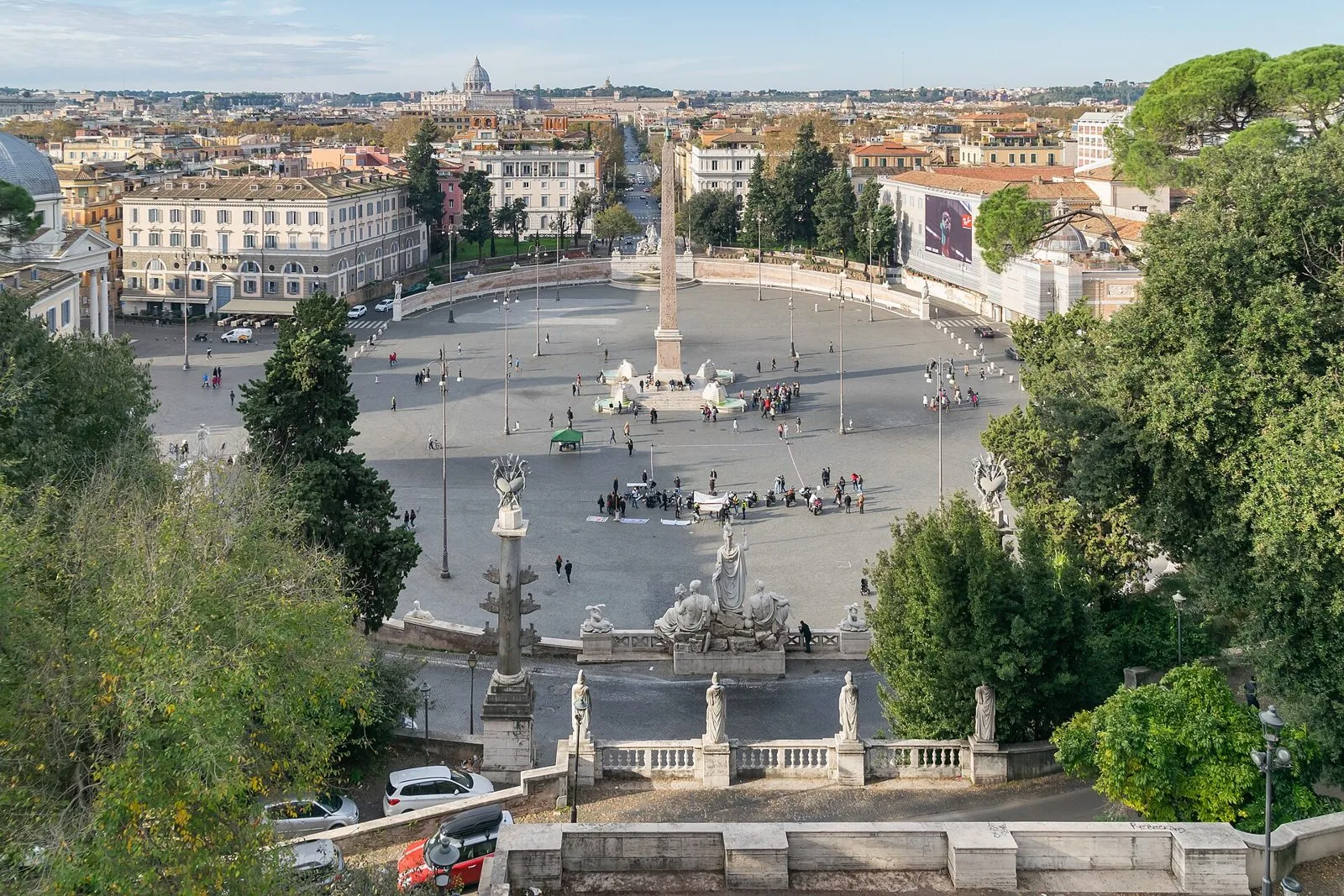 Piazza del Popolo vista dall'alto dalla terrazza del Pincio, con l'obelisco al centro, statue e balaustra in primo piano e la cupola di San Pietro all'orizzonte