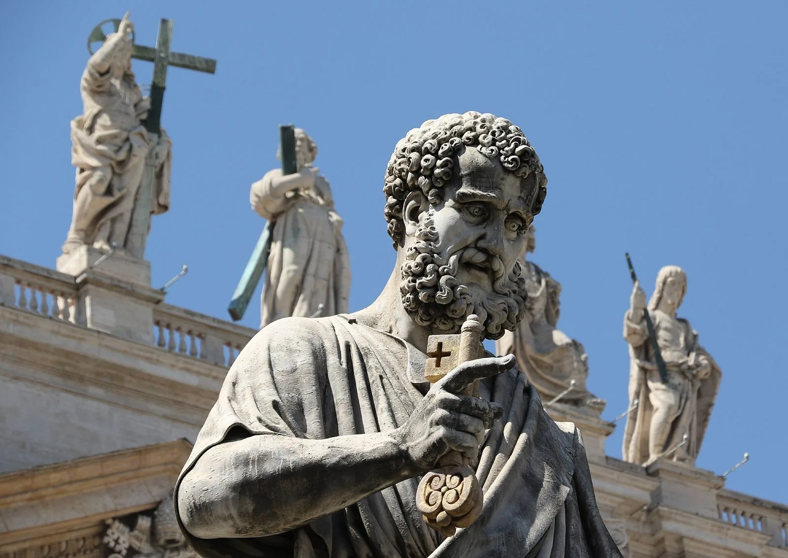 La statua in marmo di San Pietro con le chiavi in mano, davanti alla Basilica, con le statue di santi sulla balaustra e il cielo azzurro sullo sfondo