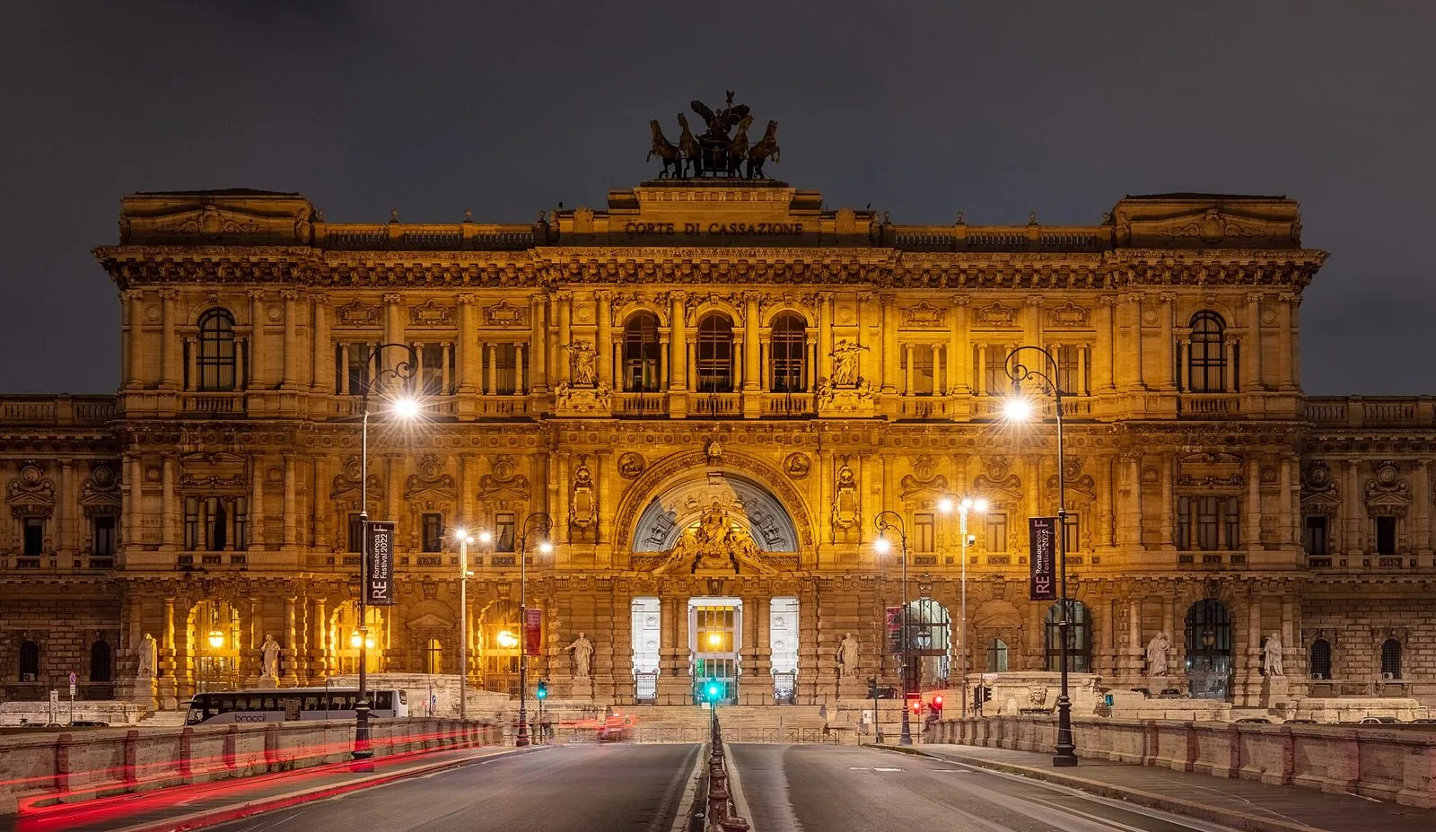 La facciata illuminata di notte del Palazzo di Giustizia di Roma, con la scritta Corte di Cassazione e la quadriga in bronzo sulla sommità, vista dal ponte